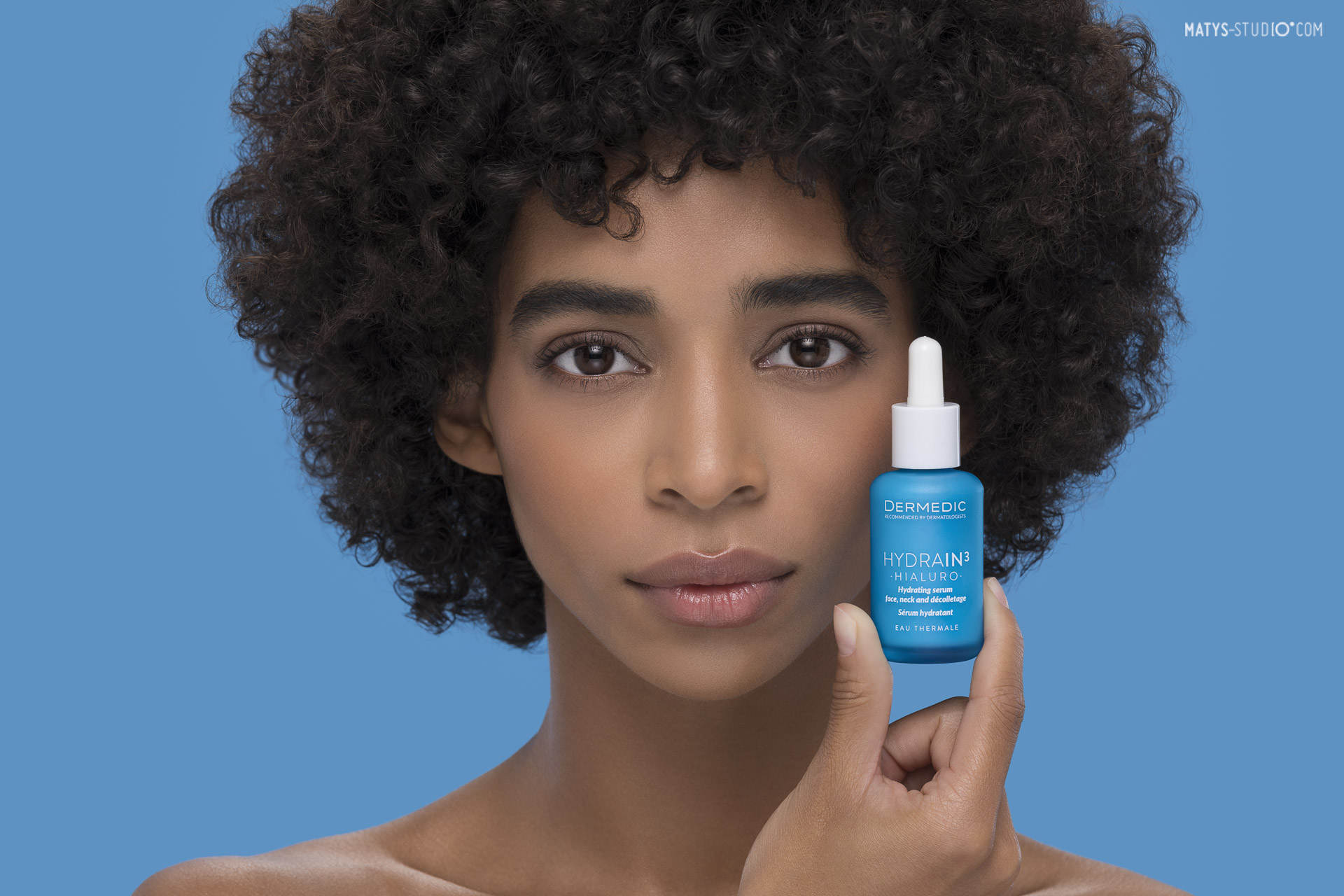 Fotografia beauty ciemnoskórej modelki trzymającej serum Dermedic blisko twarzy, sesja zdjęciowa kosmetyków.